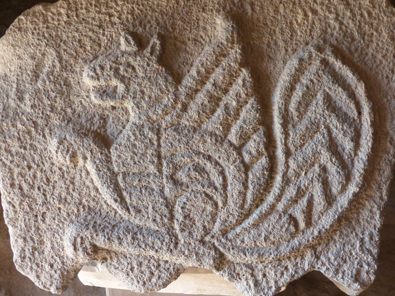 On a retrouvé des motifs animaliers de l’époque omeyyade (dynastie fondée au VIe s.) sculptés dans des blocs de basalte. Leurs thèmes sont empruntés au monde hellénistique et sassanide. Le Simorgh est une créature fabuleuse de la mythologie perse qui habite des lieux où l'eau se trouve en abondance. C’est un animal à protomé de chien, griffes de lion, muni d'une paire d'ailes et d'une queue qui remonte verticalement en se végétalisant. Les Perses sassanides associaient le Simorgh à la fertilité.
CC 4.0 Odysseum, photo F. Poli
Page à consulter :
Glossaire du Musée virtuel
Qasr al-Azraq, Simorgh sculpté.JPG