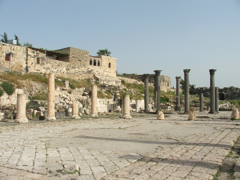 Sur ce pavement en calcaire et basalte de près de 100 m. de long s’élèvent les vestiges de colonnes corinthiennes en marbre blanc qui ornaient une basilique construite au VIe s. ap. J.-C. Les colonnes en basalte noir déterminaient un espace octogonal couvert d’un dôme. Le mur semi-circulaire derrière l’autel laisse penser que l’église servait à des pèlerinages. Elle était probablement dédiée à des saints martyrisés en 303 ap. J.-C. sous l’empereur Dioclétien (284 - 305 ap. J.-C.)
CC 4.0 Odysseum, photo F. Poli
Articles à consulter :
glossaire du Musée virtuel
Umm Qeis, la basilique.JPG