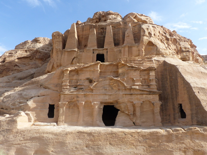 L’empilement monumental du tombeau aux Obélisques haut de 7 m. et du triclinium corinthien situé en dessous est impressionnant. Creusés dans la roche, les quatre obélisques qui ornent la façade du tombeau sont des nefesh symbolisant l’âme du défunt et ayant la même valeur qu’une statue commémorative. La façade du triclinium richement ornée ouvre l’accès à une salle réservée aux banquets et cérémonies en l’honneur des défunts inhumés dans le tombeau et dans les chambres funéraires latérales.
CC 4.0 Odysseum, photo F. Poli
Article à consulter :
glossaire du musée virtuel
Petra, le tombeau aux Obélisques et le triclinium de Bab-es-Sîq.JPG