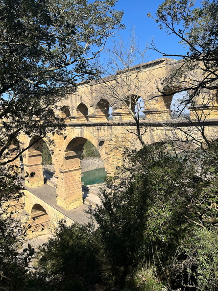 Trois arches superposées structurent le Pont du Gard. L’étage supérieur comptait 47 arceaux. L’architecte Vitruve explique dans le De architectura (VIII,7) que les voûtes réduisent le réchauffement de l’eau par le soleil. Le chantier mobilisa peut-être un millier d’hommes pendant trois à cinq ans. Les matières premières comme le bois ou les gravillons trouvées sur place permirent de fabriquer des matériaux transformés comme la chaux ou le mortier nécessaires au scellement des piliers inférieurs.
Photos CC 4.0 Odysseum, classe de P. Cochet Terrasson 2025
Articles à consulter :
Vitruve - Le Pont du Gard - Glossaire du musée virtuel
Pont du Gard, les trois rangées d'arches.jpg