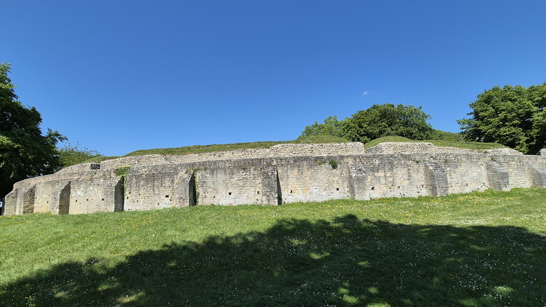 Les gradins de la cauea reposent sur un talus de terre rapportée qui est entouré un mur semi-circulaire d’environ 5 m de haut (praecinctio). Il est composé de petits moellons de pierres locales réunis par un mortier très dur. Pour soutenir ce mur contre la poussée des gradins et lui assurer la résistance suffisante, il est renforcé de trente contreforts. Lors des fouilles menées au XIXe s., on a retrouvé dans le théâtre des pièces à l’effigie de l’empereur Antonin le Pieux (138 - 161 ap. J.-C.).
Photo CC 4.0 Odysseum, F. Poli
Articles à consulter :
Architecture du théâtre - Empereurs romains - Glossaire
Champlieu, le mur extérieur du théâtre .jpg