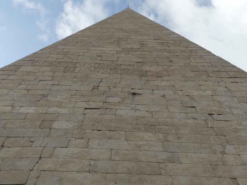 Deux inscriptions sont gravées sur la face sud-ouest. La première, sur la partie haute de la pyramide, a permis de comprendre à qui était destiné le tombeau : « C. Cestius L.F. Pob. Epulo pr. tr.pl. VII vir epulonum », ce qui signifie « Caius Cestius Epulo, fils de Lucius, de la tribu Poblilia, préteur, tribun de la plèbe, membre du collège des septemviri epulones (chargés de veiller aux grands festins sacrés). » La titulature témoigne de la carrière et de l’importance du personnage.
Photo CC 4.0 Odysseum, F.Poli
Article à consulter :
Glossaire
Rome - Pyramide de Cestius, inscriptions sur la Pyramide de Cestius.JPG